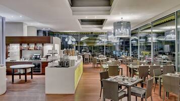 A modern restaurant interior with a central bar area, dining tables, and chairs.