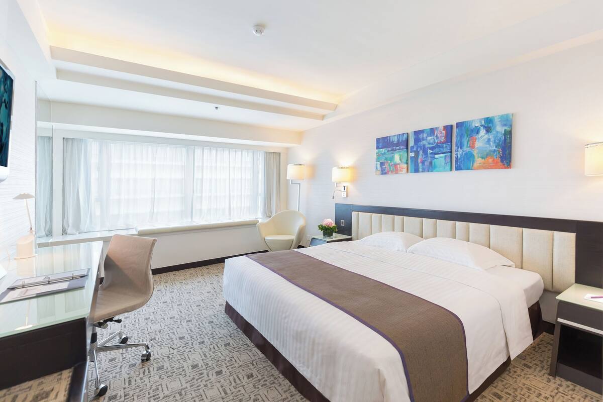 Habitación de hotel con una cama grande, un escritorio con silla, un televisor y obras de arte en la pared.