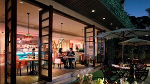An outdoor dining area with tables and chairs, a pool, and a restaurant with a chef in the background. - Regal Riverside Hotel (Sha Tin)