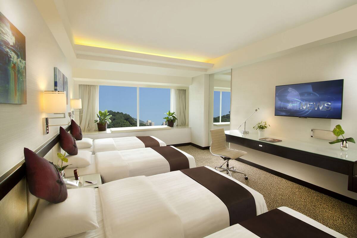 Habitación de hotel con dos camas, un escritorio, un televisor y un ventanal con vistas.