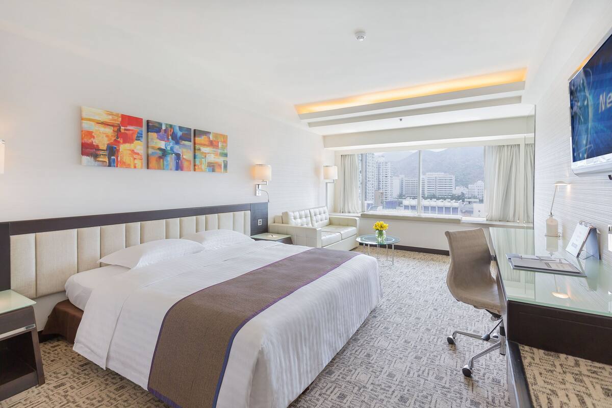 Habitación de hotel con una cama grande, un escritorio, una silla, un televisor y vistas a la ciudad.