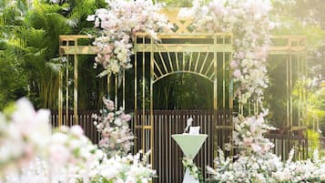 A garden wedding arch with white flowers and a white table in the foreground.