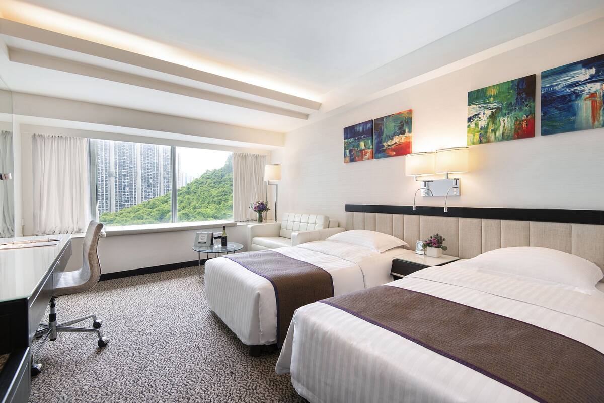 Habitación de hotel con dos camas, un escritorio, una silla, una lámpara y obras de arte en la pared.