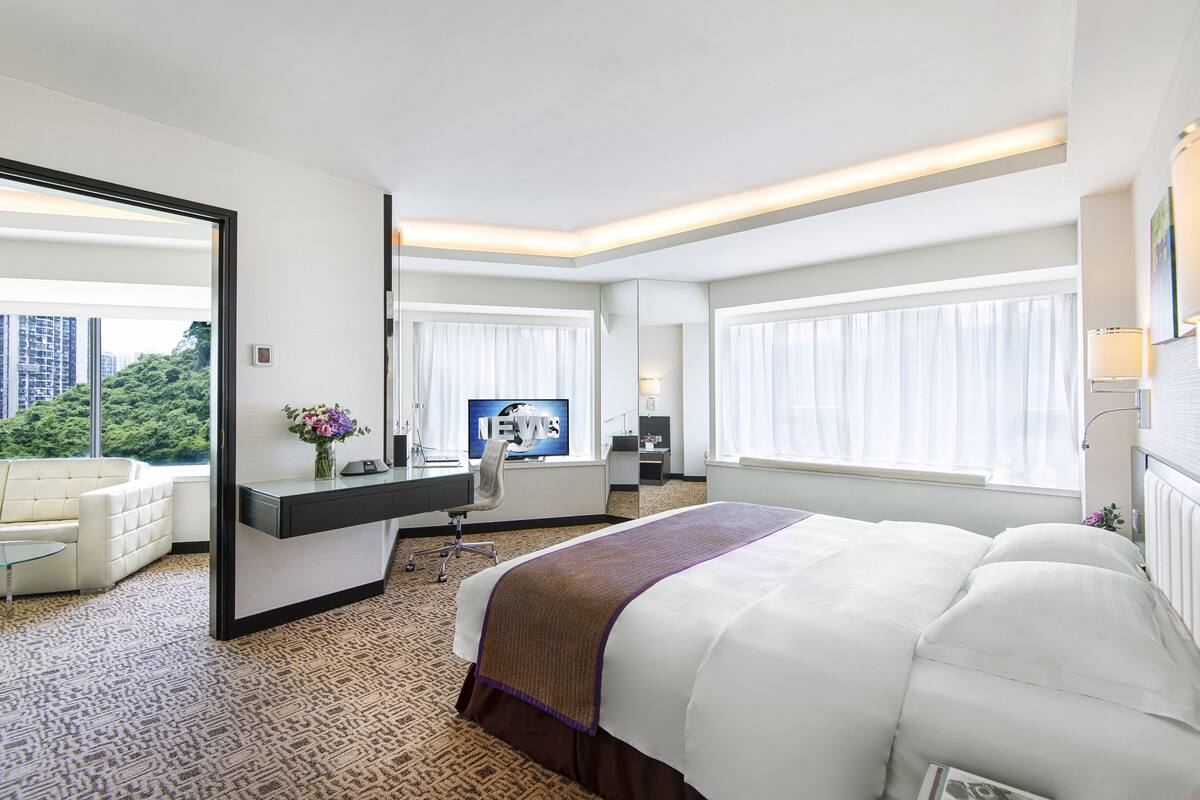 Habitación de hotel con una cama grande, un escritorio con silla, televisión y vistas a zonas verdes.