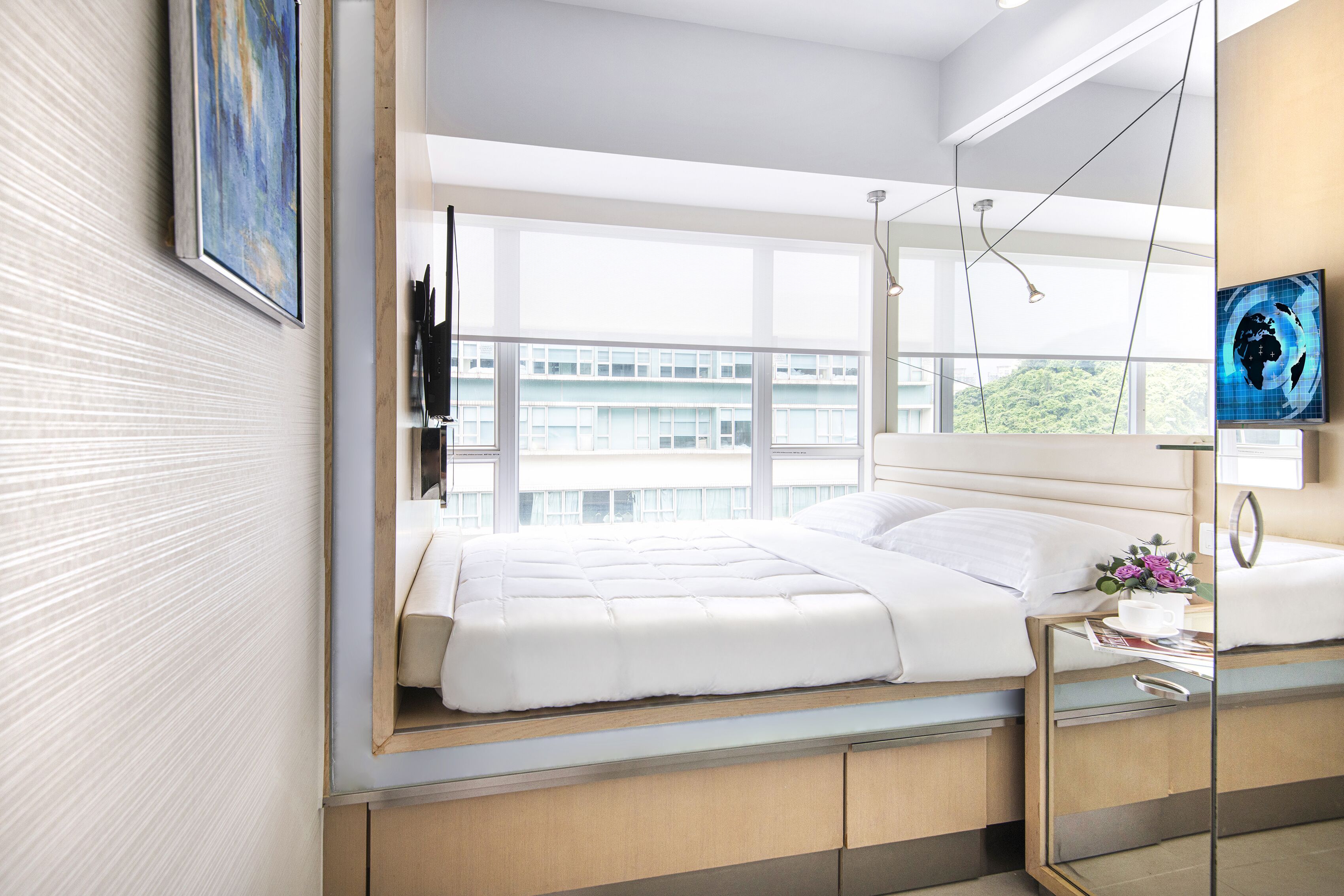 A modern hotel room with a bed, bedside table, and a large window offering a city view.