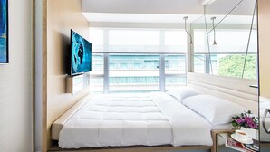 A modern bedroom with a large bed, a television on the wall, and a view of a building through the window. - Regal Riverside Hotel (Sha Tin)