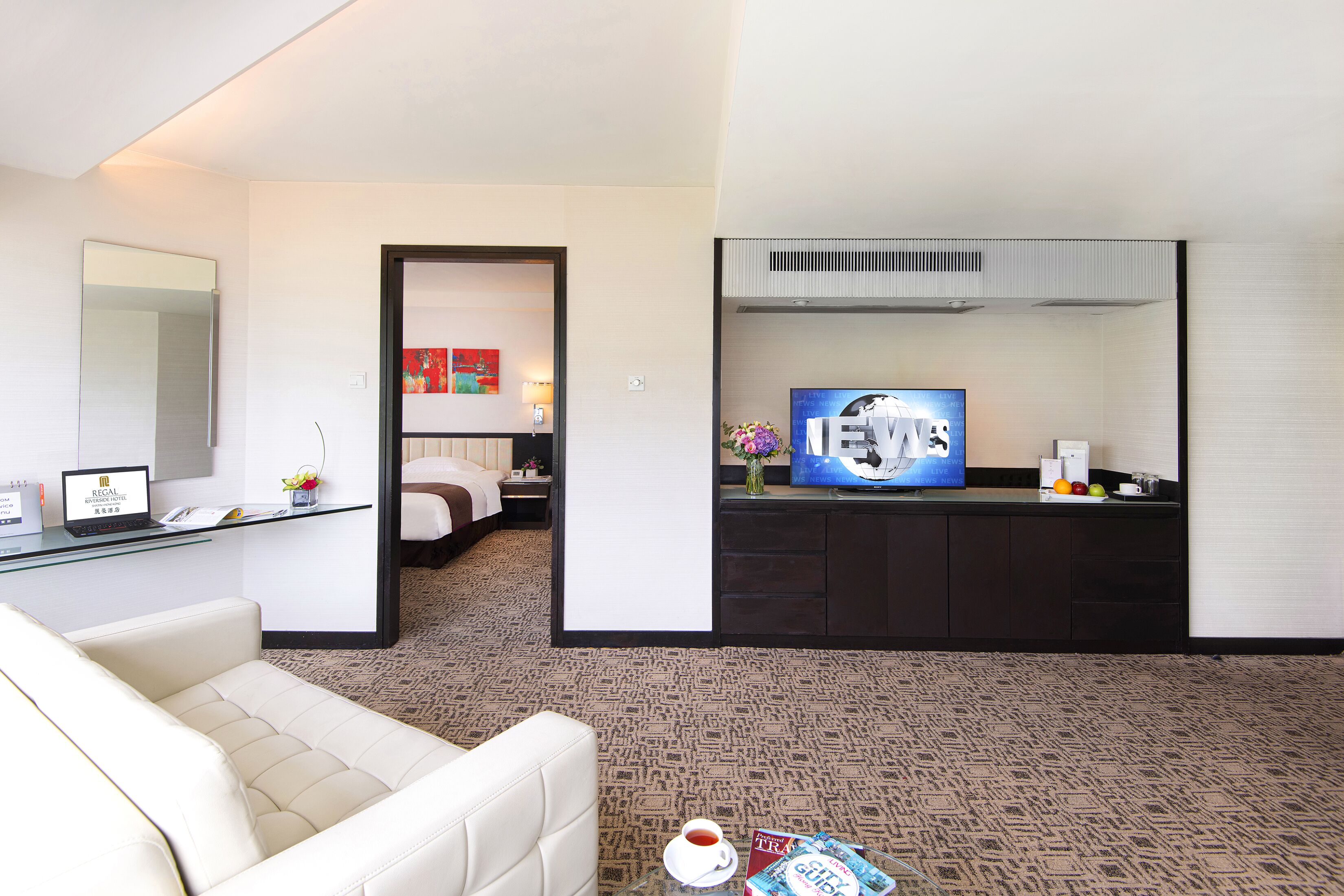Habitación de hotel con sofá, escritorio con laptop, televisión y pequeña cocina.