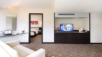 Habitación de hotel con sofá, escritorio con laptop, televisión y pequeña cocina.