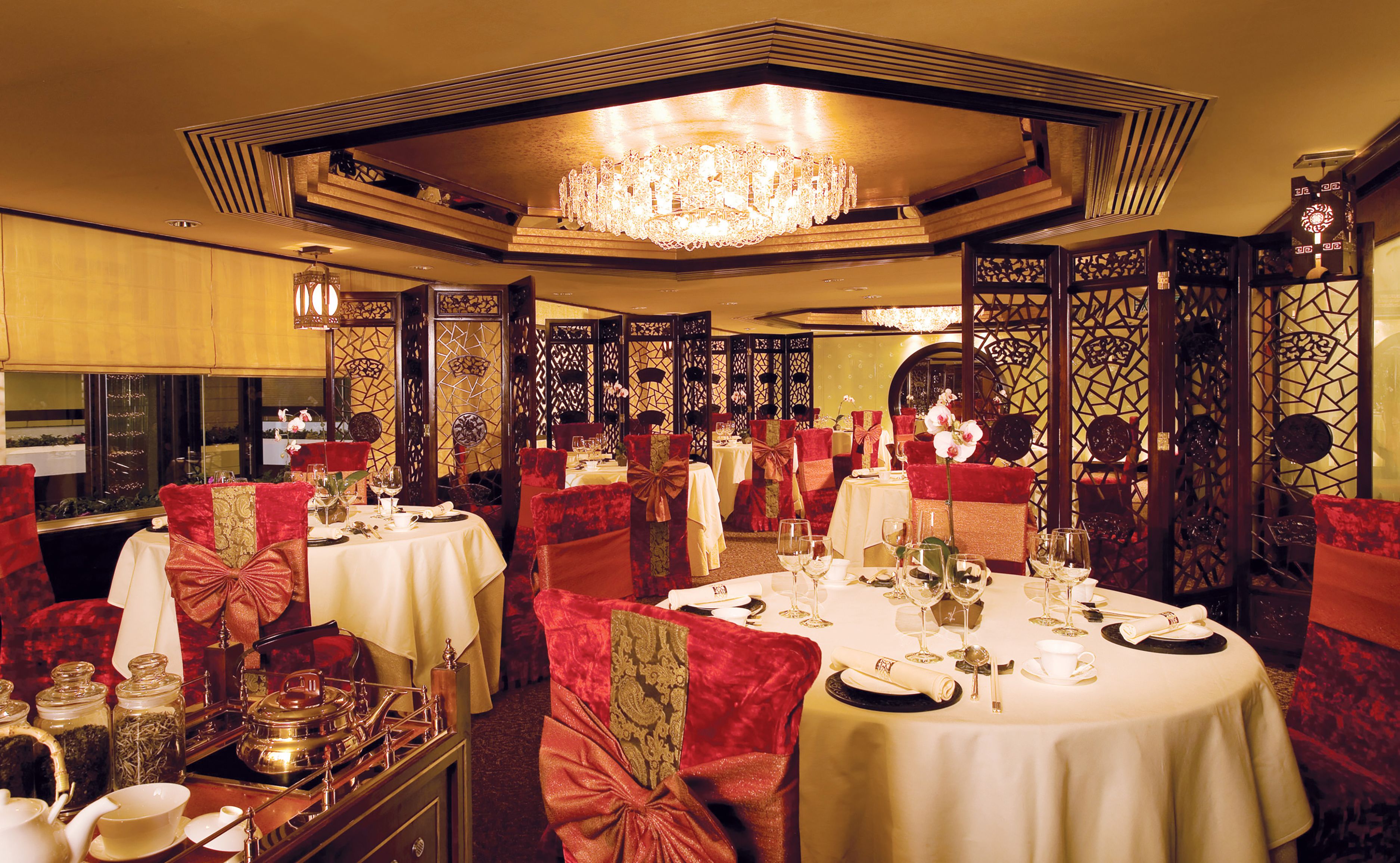 Una sala da pranzo formale con tavoli apparecchiati, eleganti sedie e un lampadario.