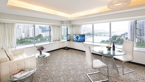 A modern hotel room with a city view, a glass table, white furniture, and a large TV. - Regal Riverside Hotel (Sha Tin)