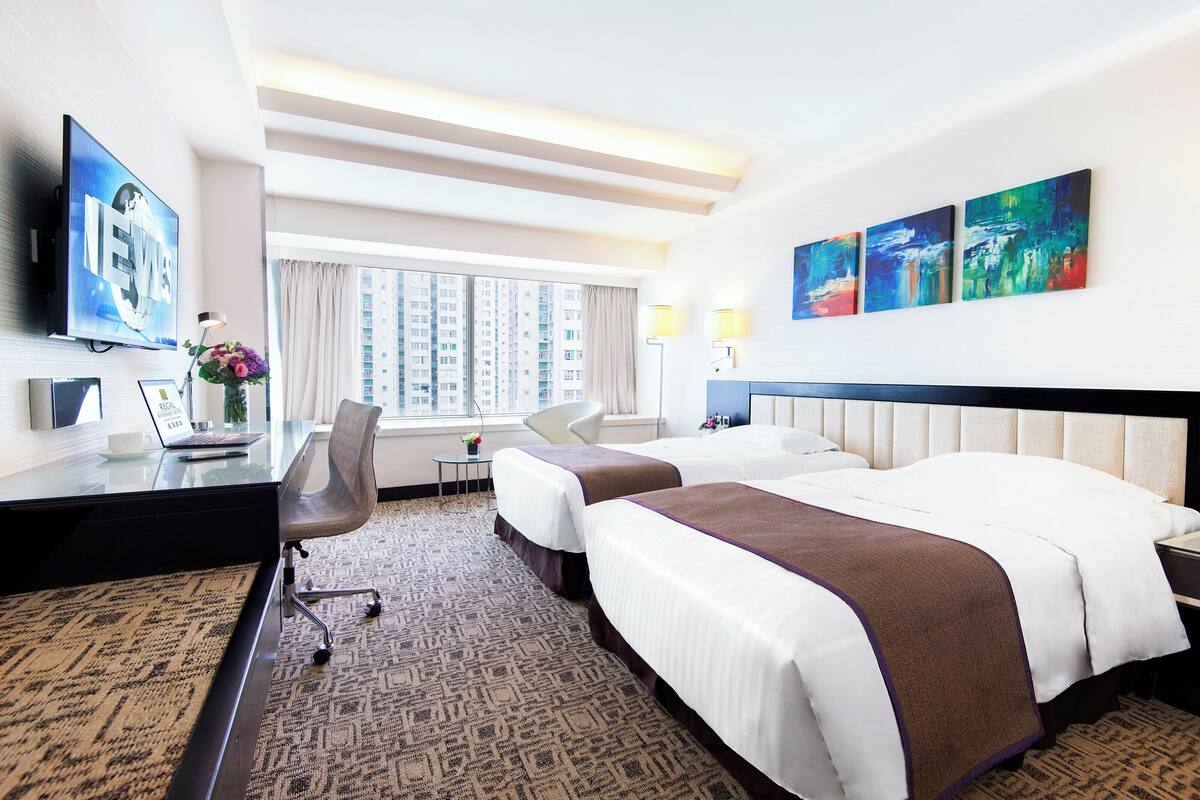 Habitación de hotel con dos camas, un escritorio con una computadora portátil, un televisor y obras de arte en la pared.