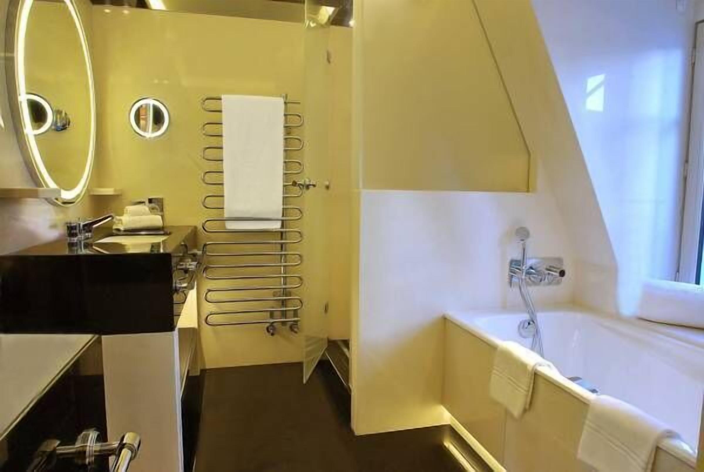 A compact, modern bathroom with a bathtub, a towel rack, and a mirror with a light.