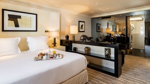 Quarto de hotel com uma cama grande, uma mesa de cabeceira com uma bandeja de itens de café da manhã, uma escrivaninha com abajur e um espelho refletindo o quarto.