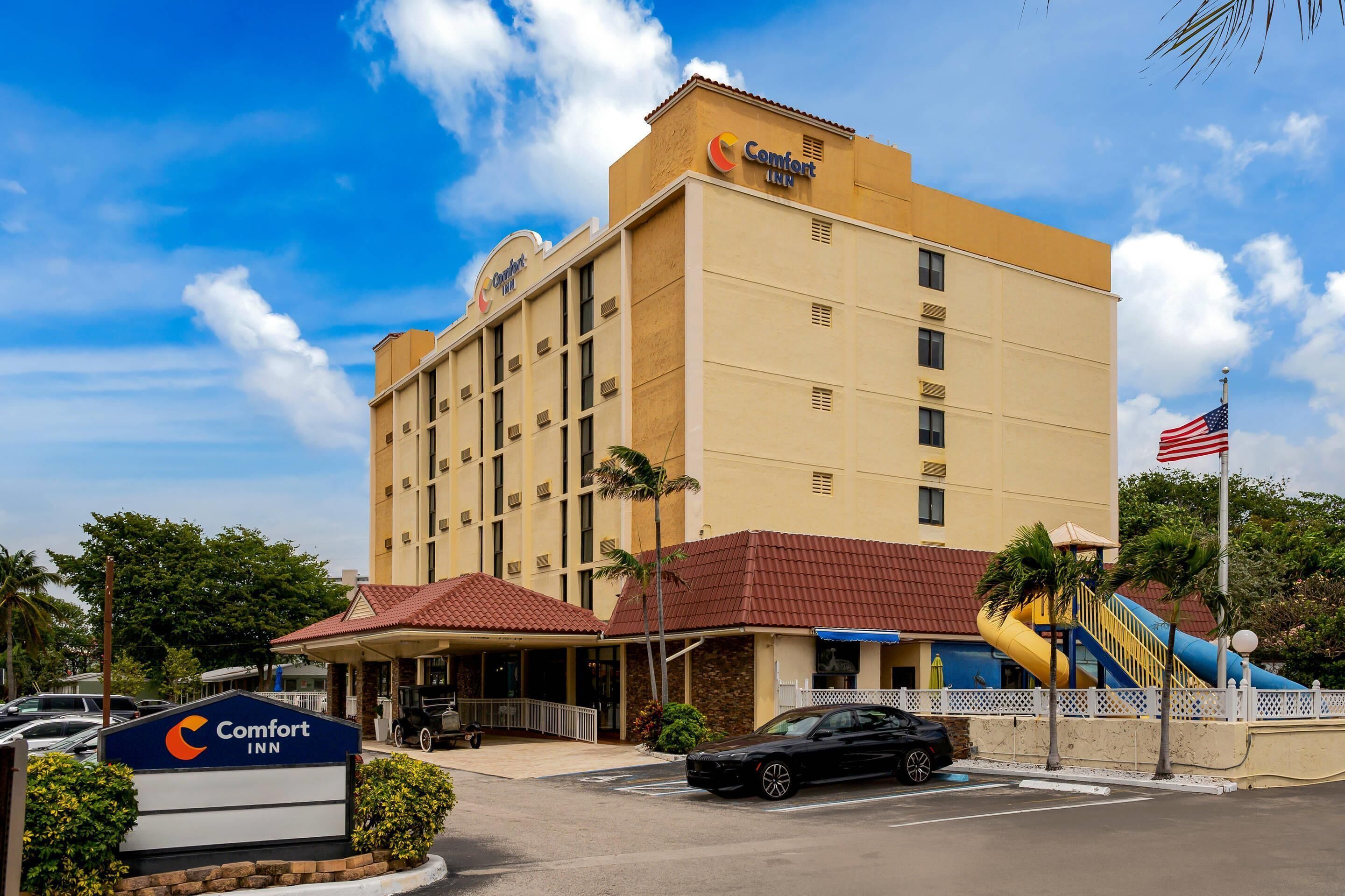 A Comfort Inn hotel with a red-roofed entrance, a parking lot, and a playground with slides.