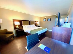 A hotel room with a bed, a desk, a chair, a TV, and a desk lamp. - Comfort Inn Oceanside Deerfield Beach (Deerfield Beach)