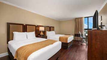 Ein Hotelzimmer mit zwei Betten, einem Schreibtisch, einem Stuhl und einem großen Fenster mit Vorhängen.