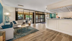A modern hotel lobby with a seating area, a reception desk, and large glass doors leading to the parking area. - Comfort Inn Oceanside Deerfield Beach (Deerfield Beach)