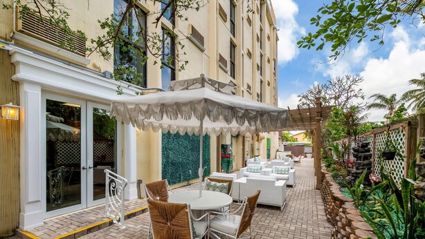 An outdoor patio with white wicker furniture, a covered seating area, and a stone wall with plants. - Comfort Inn Oceanside Deerfield Beach (Deerfield Beach)