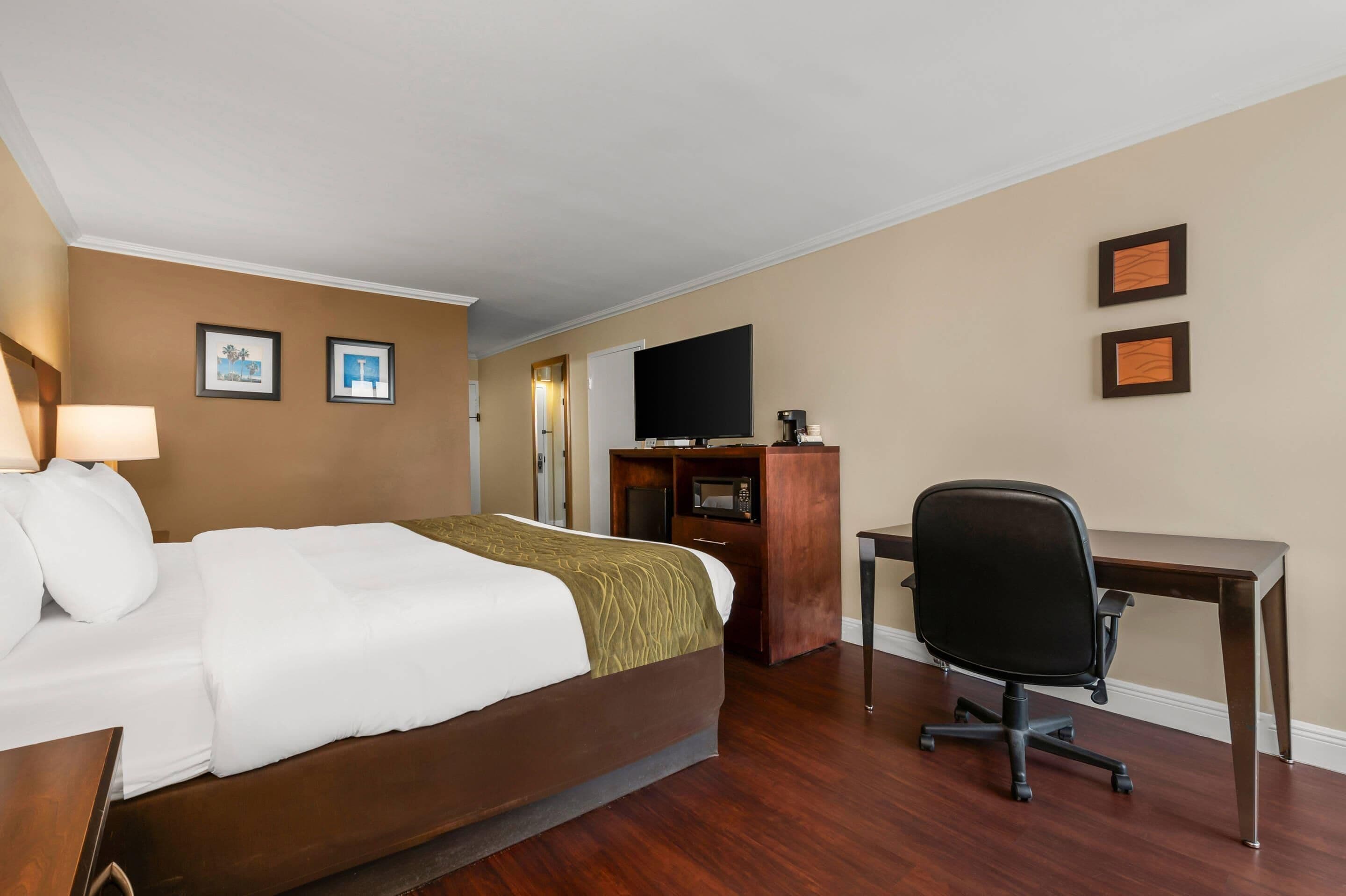 A hotel room with a bed, desk, chair, TV, and a minibar.