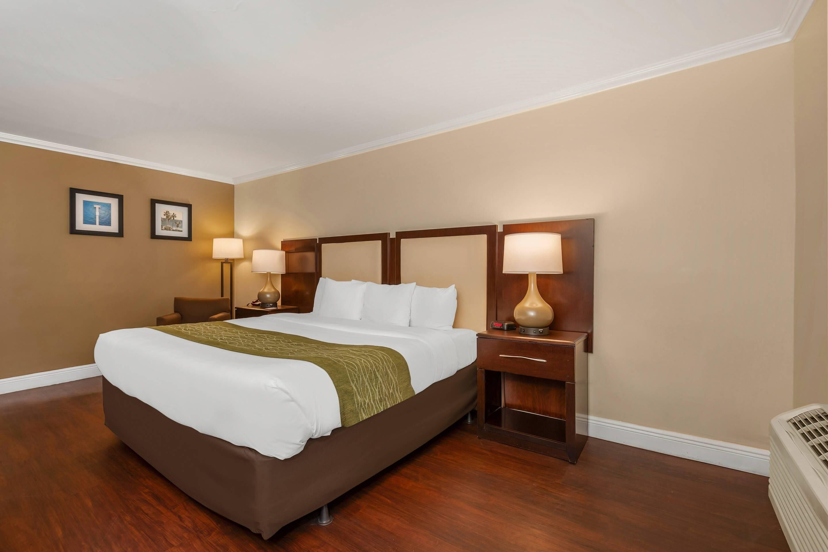 A hotel room with a large bed, two bedside tables with lamps, a heater, and two framed pictures on the wall.