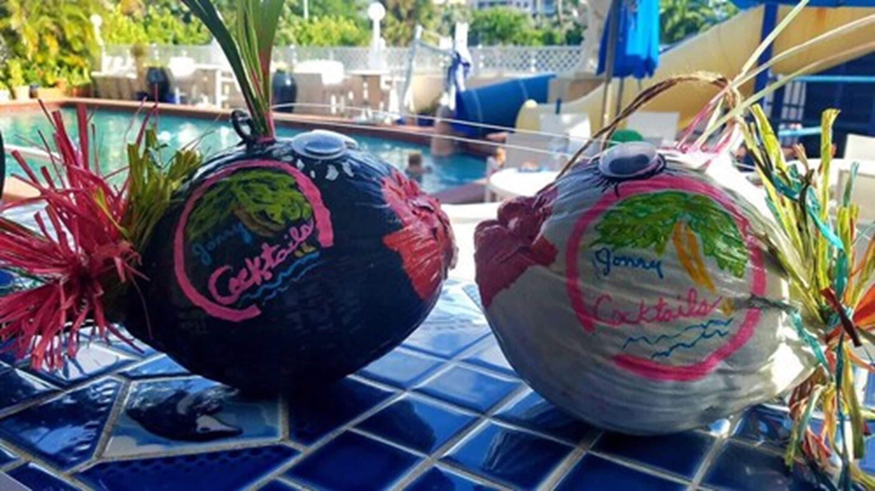 Deux agitateurs à cocktails décorés sont posés sur une surface carrelée, près d’un espace piscine.