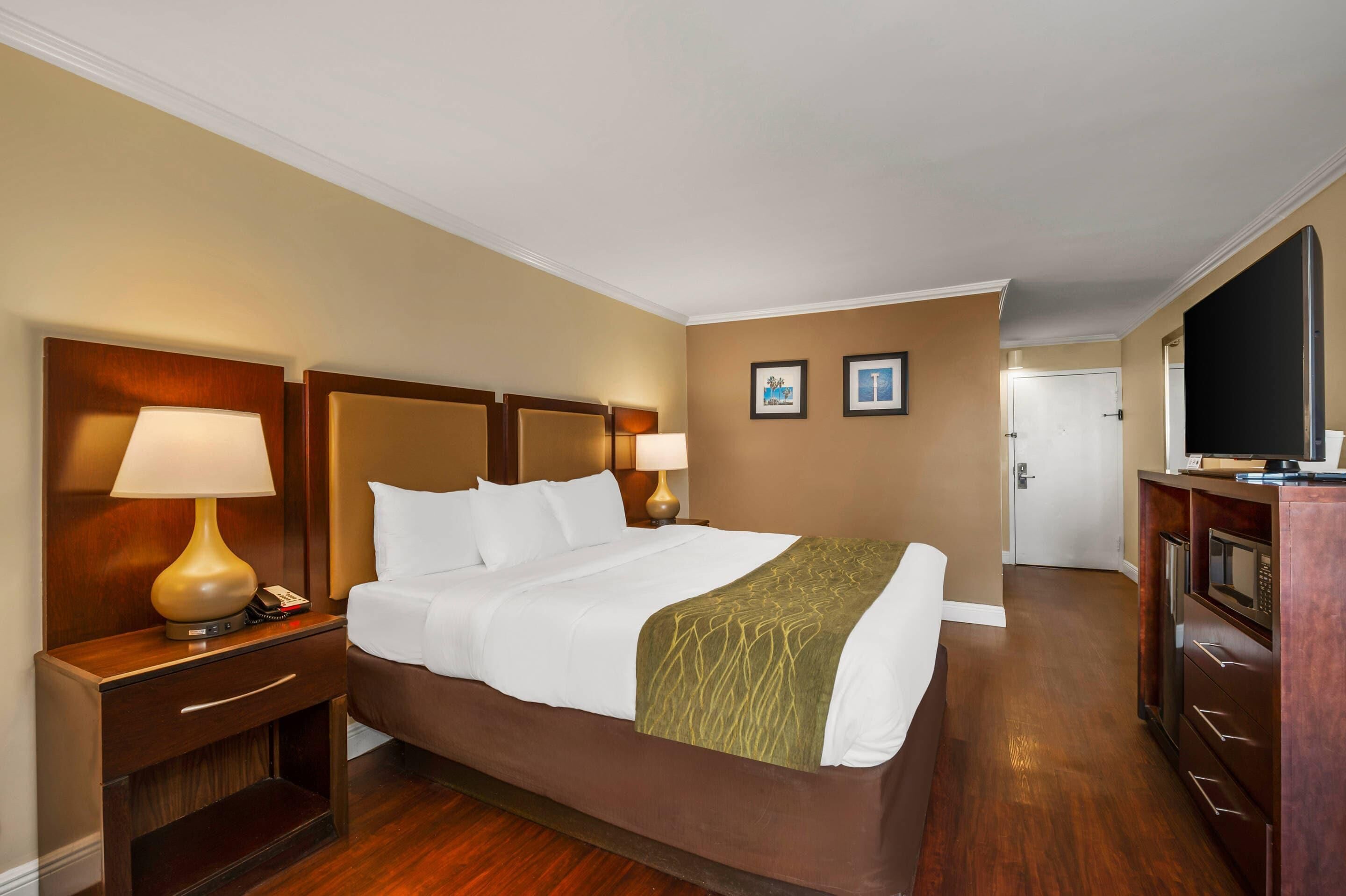 Habitación de hotel con una cama grande, dos lámparas de noche, un cabecero de madera, un televisor y un minibar.