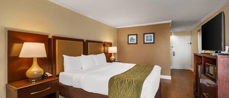 A hotel room with a large bed, two bedside lamps, a wooden headboard, a television, and a minibar.