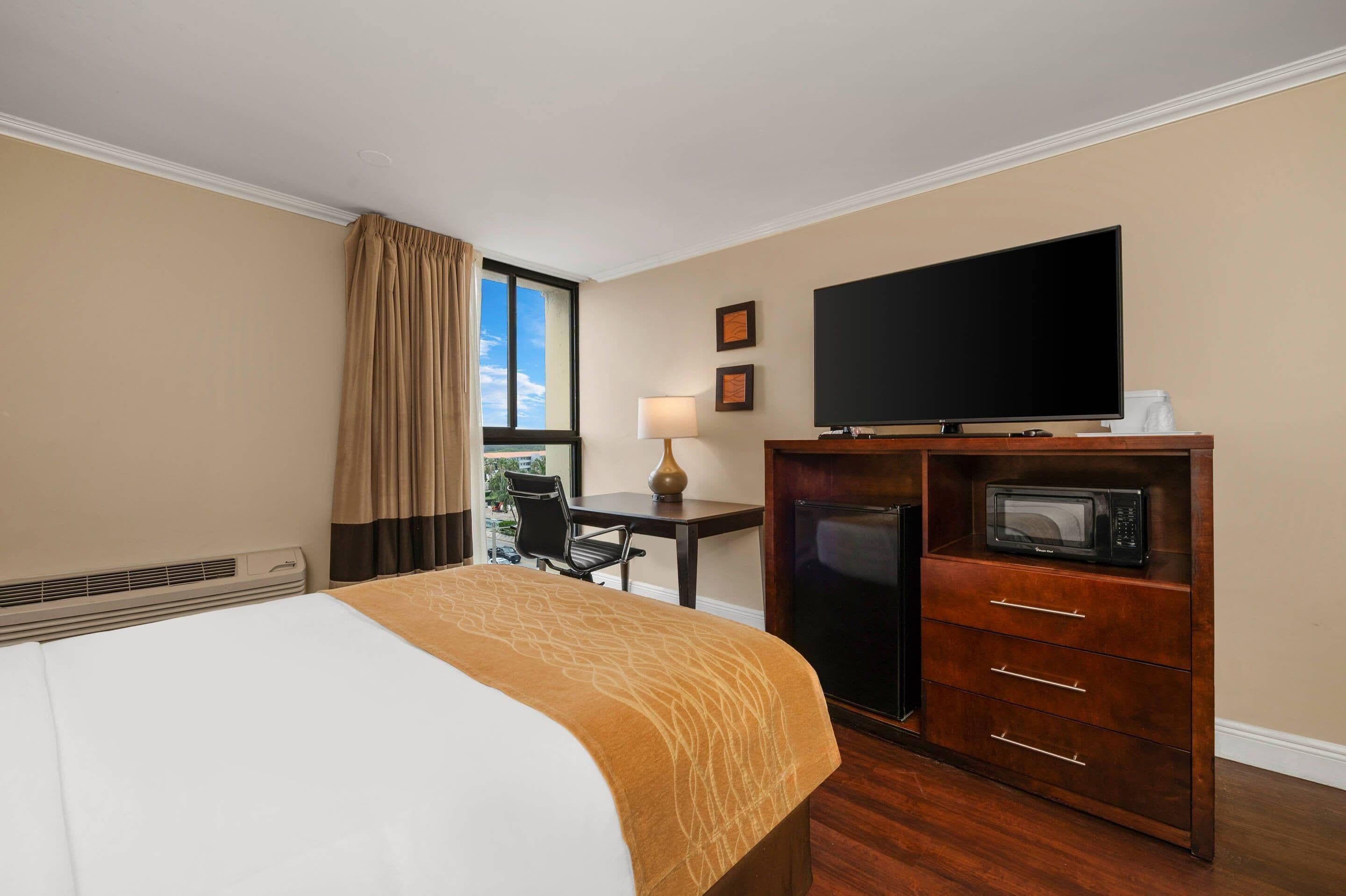 A hotel room with a bed, a desk, a television, and a microwave.