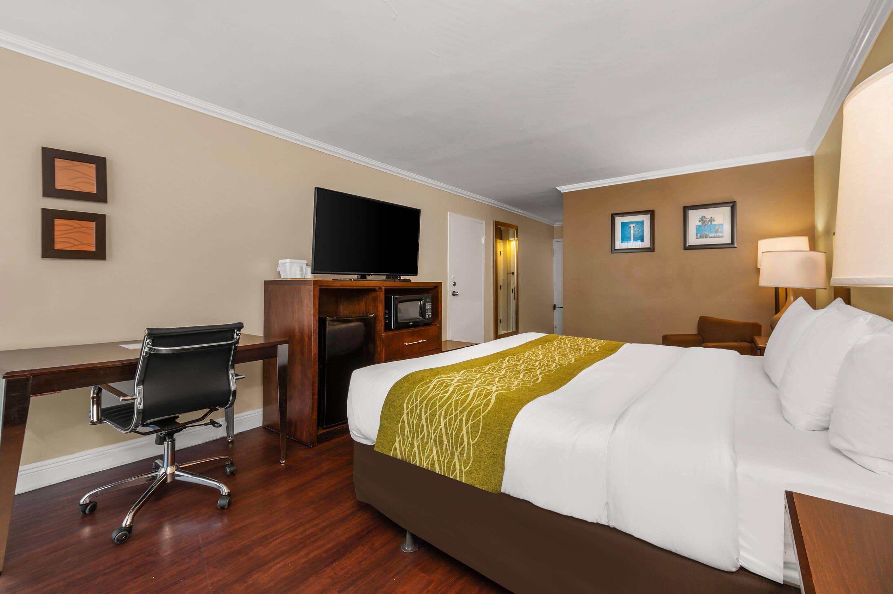A hotel room with a bed, a desk, a chair, a television, and a lamp.