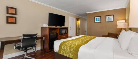 A hotel room with a bed, a desk, a chair, a television, and a lamp.