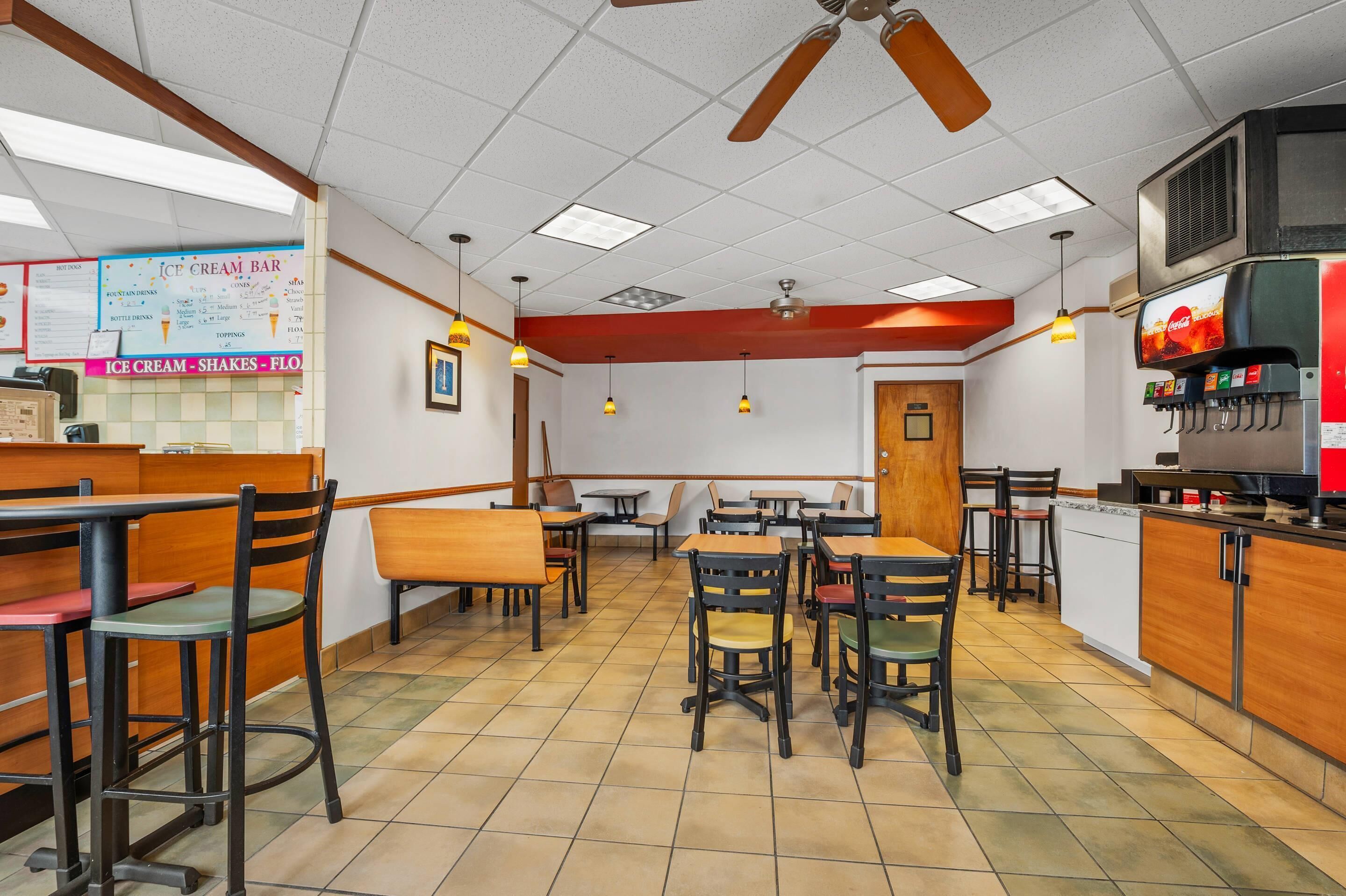 A restaurant interior with booths and tables, a menu board, and a beverage dispenser.