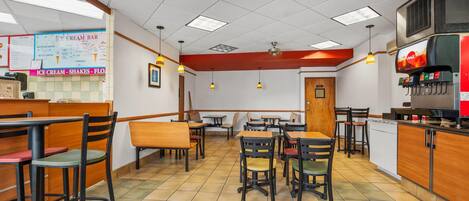 A restaurant interior with booths and tables, a menu board, and a beverage dispenser.