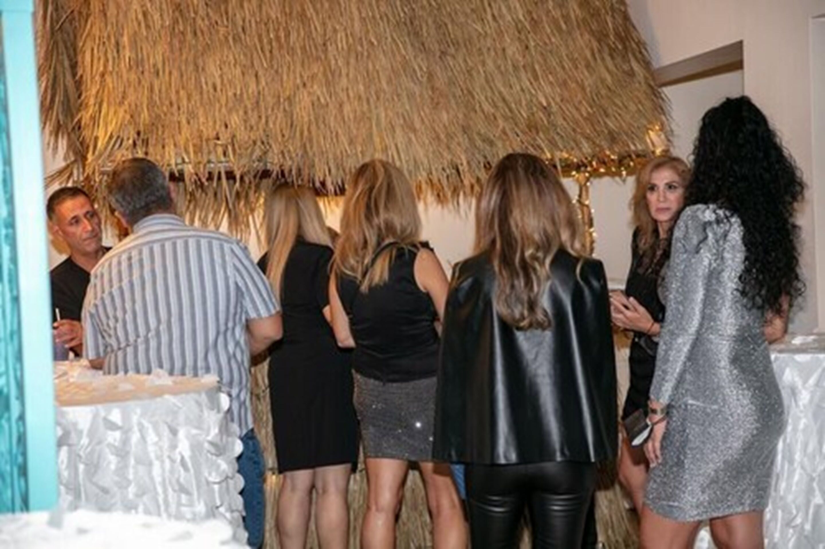 A group of people standing in a room with a thatched ceiling and white walls.