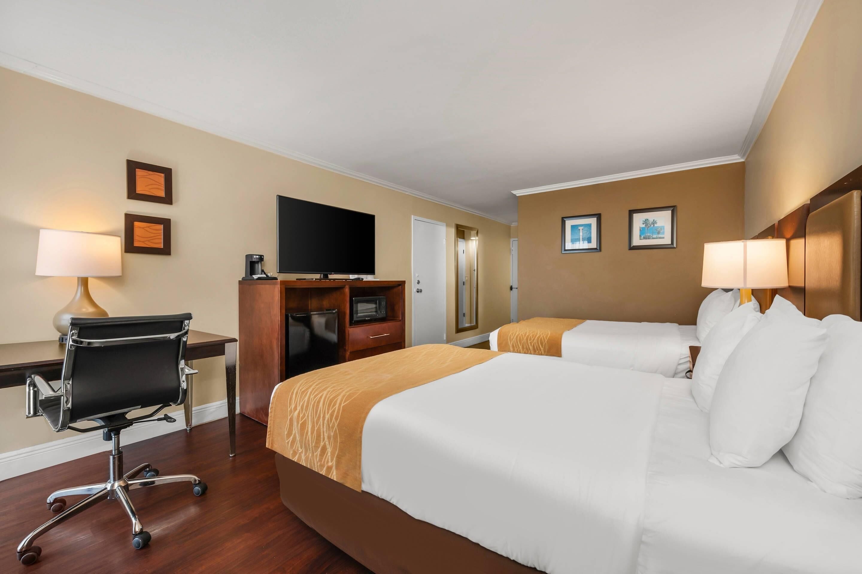 A hotel room with two beds, a desk, a chair, a television, and a coffee maker.