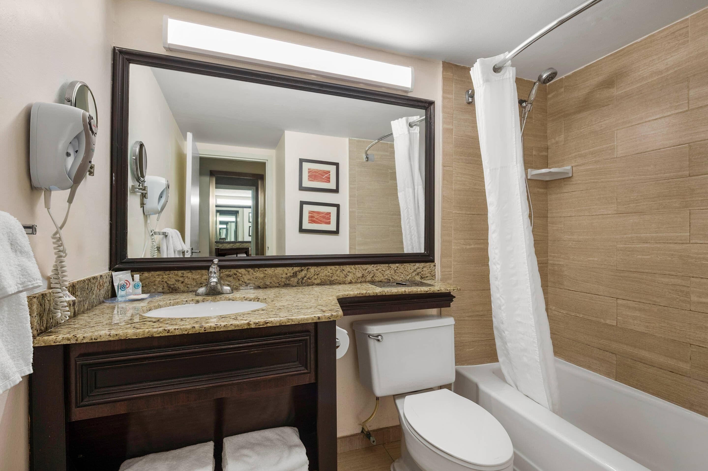 A bathroom with a granite countertop sink, a dark wood vanity, a white toilet, and a shower with a white curtain.