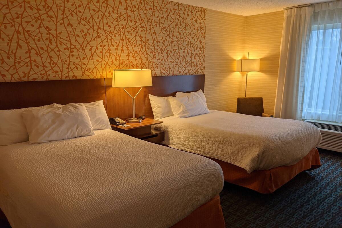 A hotel room with two beds, a nightstand with a lamp, a telephone, and a wall with a leaf pattern.