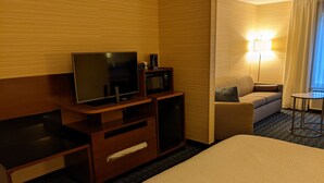 A hotel room with a bed, a desk with a television and a microwave, a sofa, a small table, and a lamp. - Fairfield Inn By Marriott Concord (Concord)