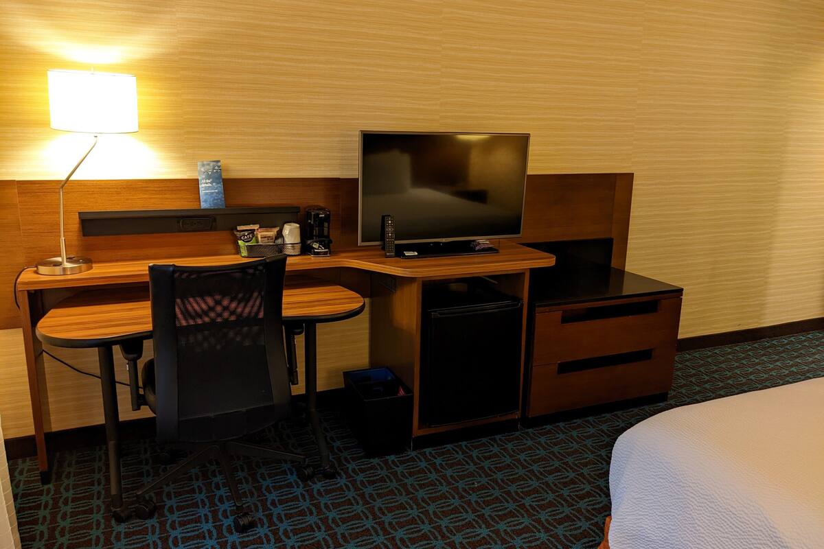 A hotel room with a desk, chair, television, and a bed.
