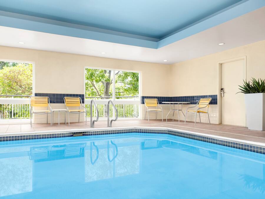 A swimming pool with chairs and a potted plant, surrounded by windows and a door.