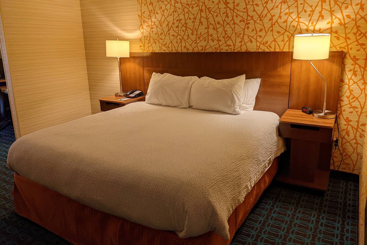 A hotel room with a large bed, two bedside tables, a telephone, and two lamps.