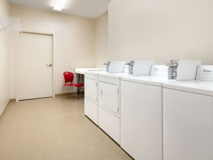 A laundry room with white appliances, a red chair, and a door.