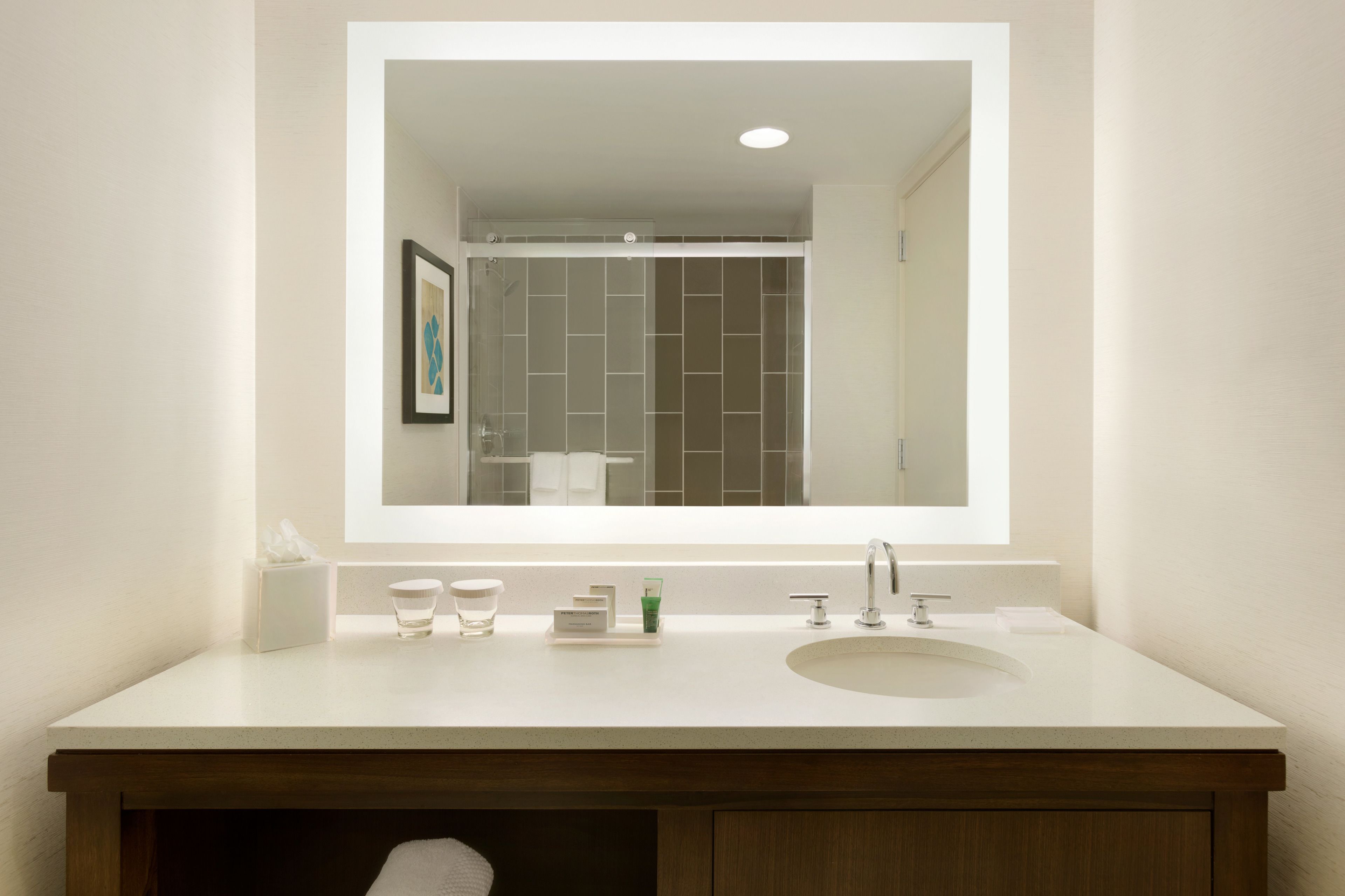 A bathroom with a large mirror, a sink, and a shower area.