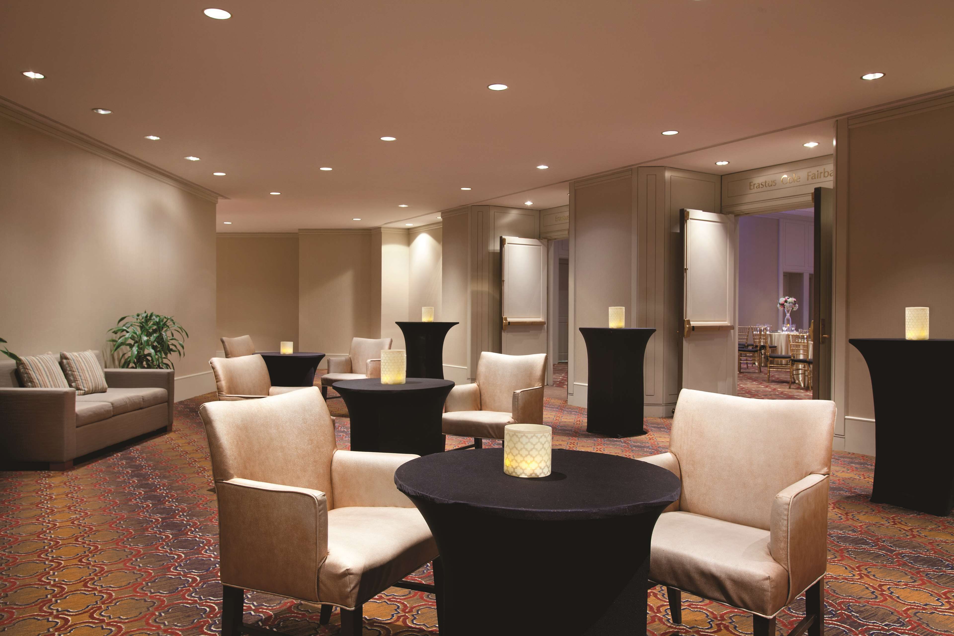 Um hall de hotel com sofá, poltronas, uma mesa redonda e piso coberto de carpete.