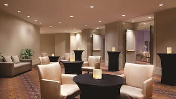 Um hall de hotel com sofá, poltronas, uma mesa redonda e piso coberto de carpete.