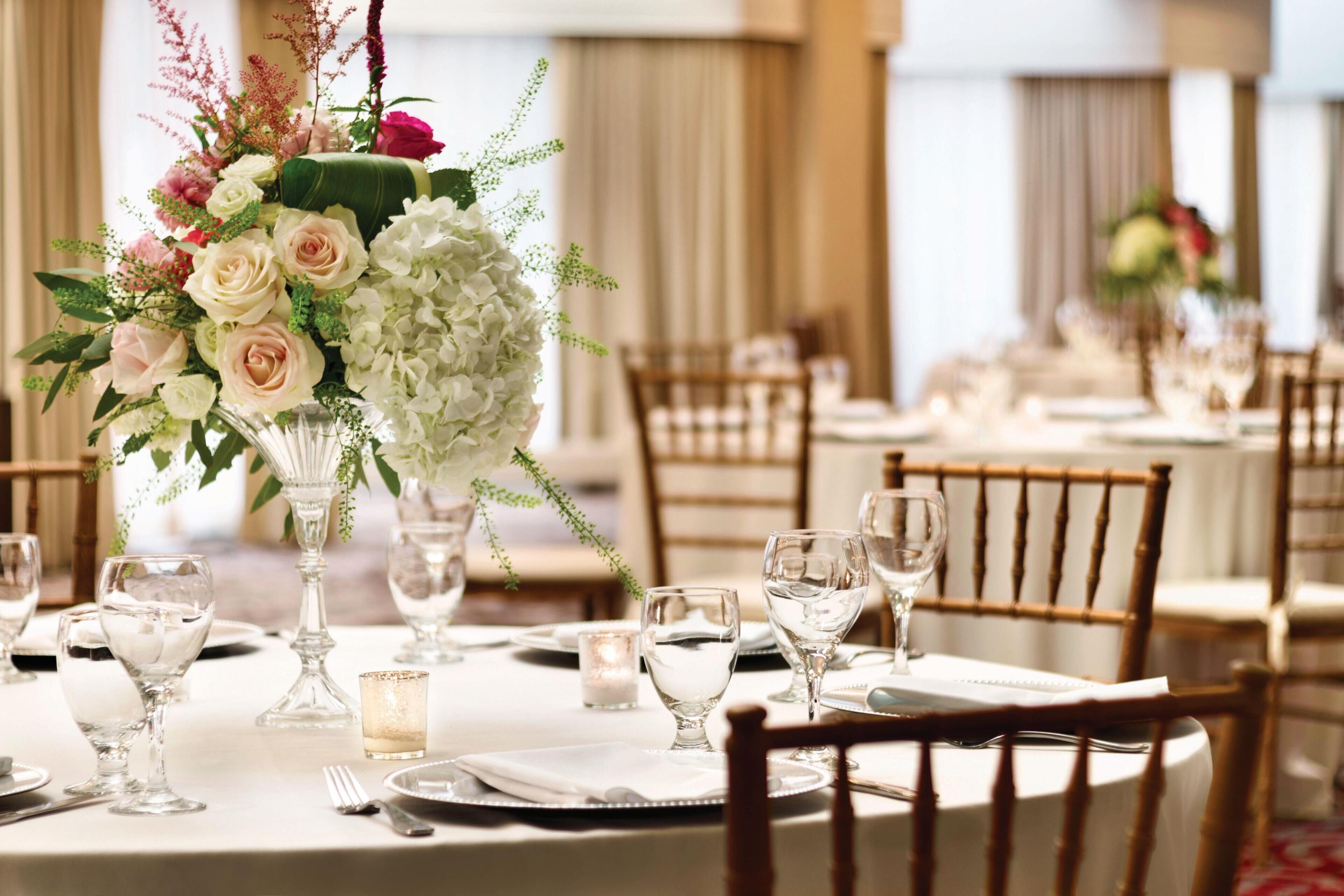 Una mesa de banquete dispuesta para un evento formal, con cristalería, platos y un centro de mesa con flores.