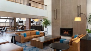 A spacious lobby with a high ceiling, a fireplace, and a seating area with sofas and tables. - Hilton Boston/Dedham (Dedham)
