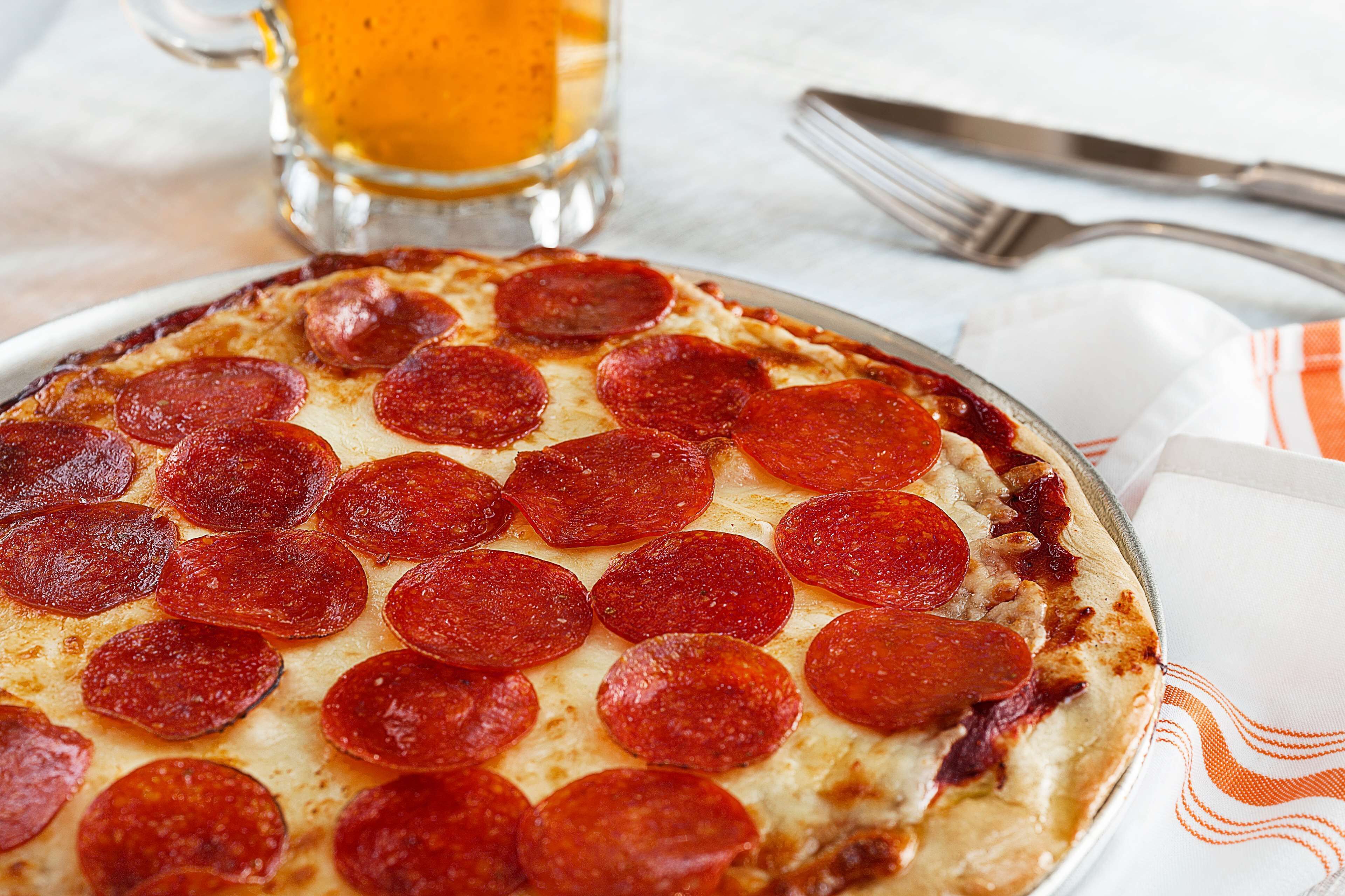 Eine Pizza Salami auf einem Teller, im Hintergrund ein Glas Bier.