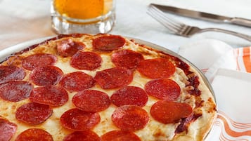 Eine Pizza Salami auf einem Teller, im Hintergrund ein Glas Bier.