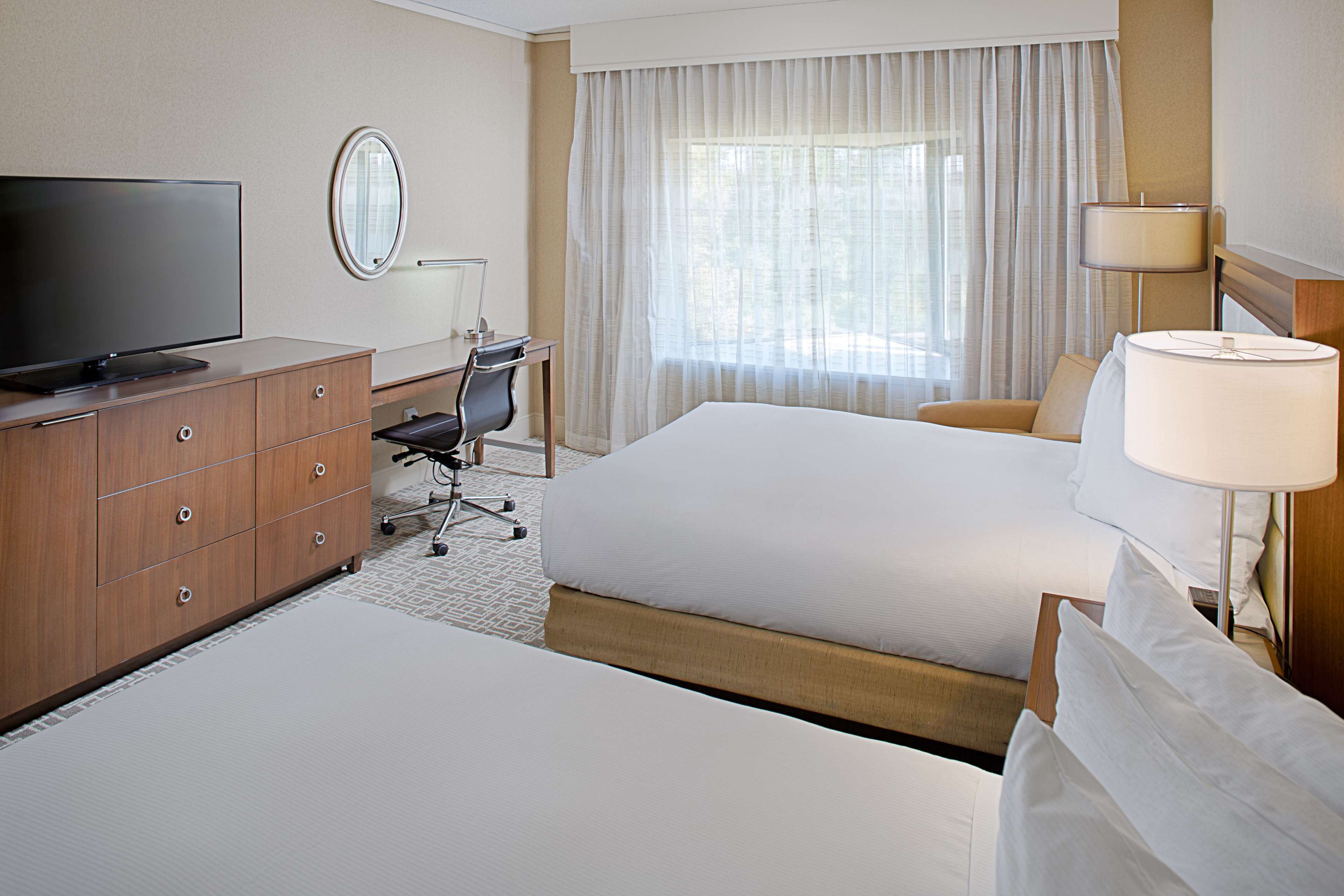 A hotel room with two beds, a desk with a chair, a television, and a lamp.