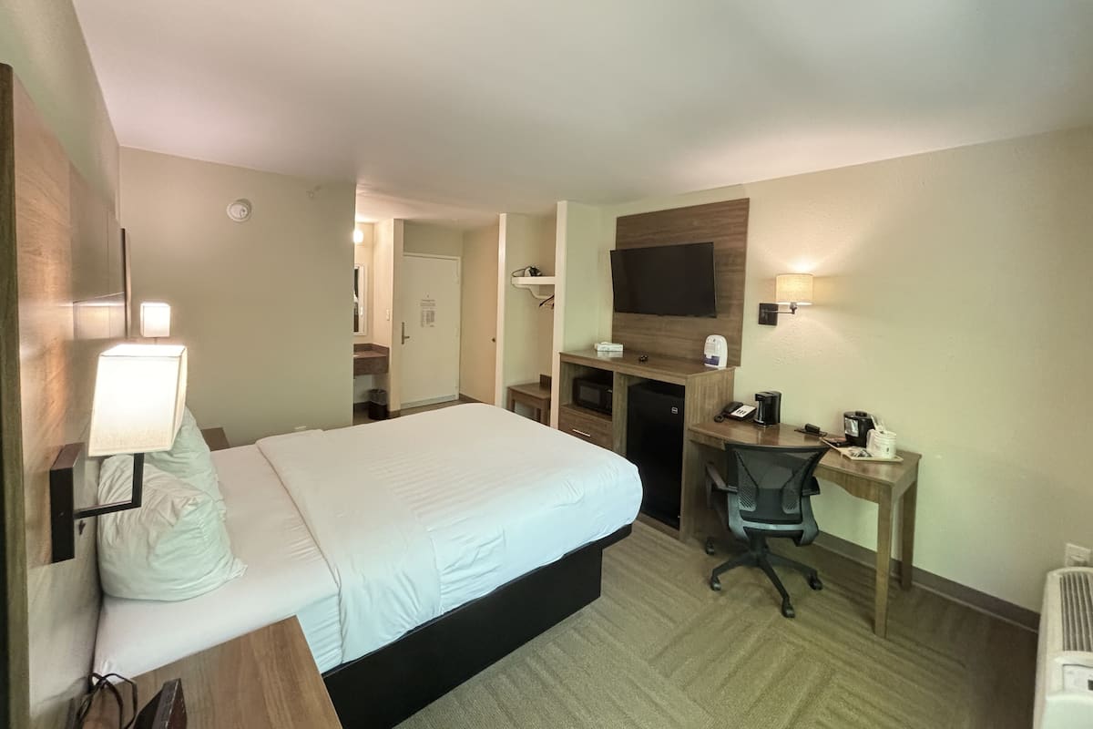 Une chambre d’hôtel équipée d’un lit, d’un bureau, d’une chaise, d’une télévision et d’une petite kitchenette.